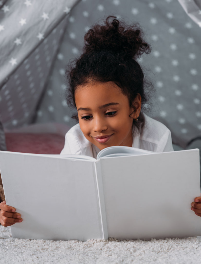 adorable african american kid reading book and lying in tent at home